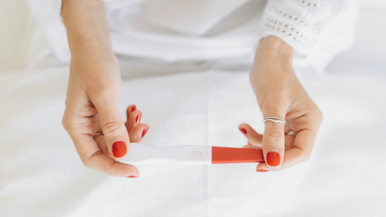 12 week ultrasound: Woman in white holding a positive pregnancy test in soft bright light