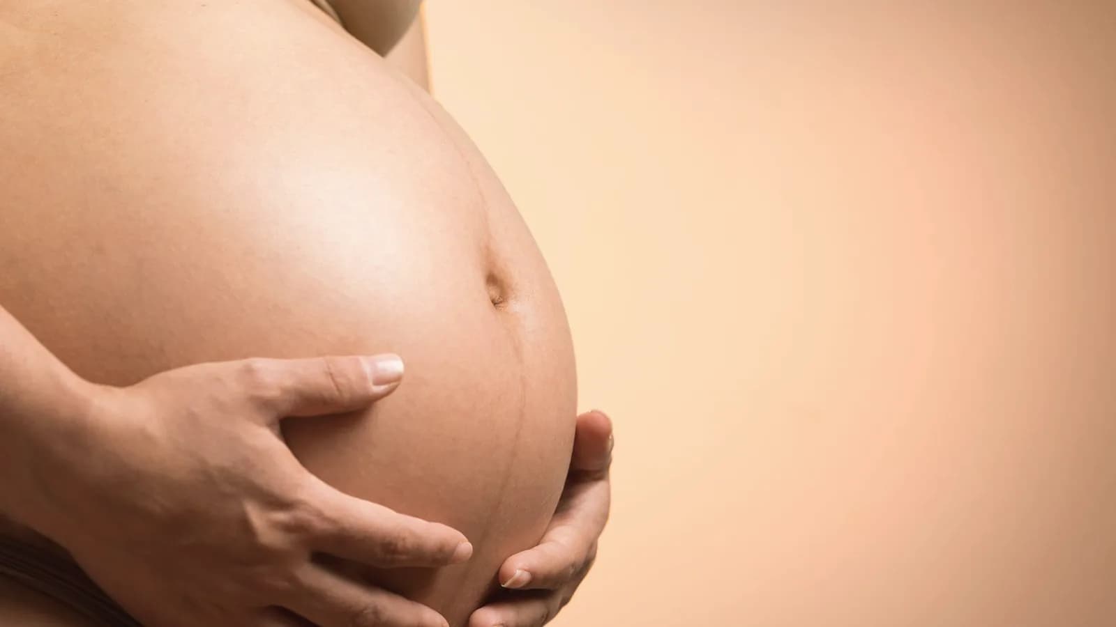 32 weeks pregnant baby features: Close up of a pregnant belly held gently by both hands in warm light