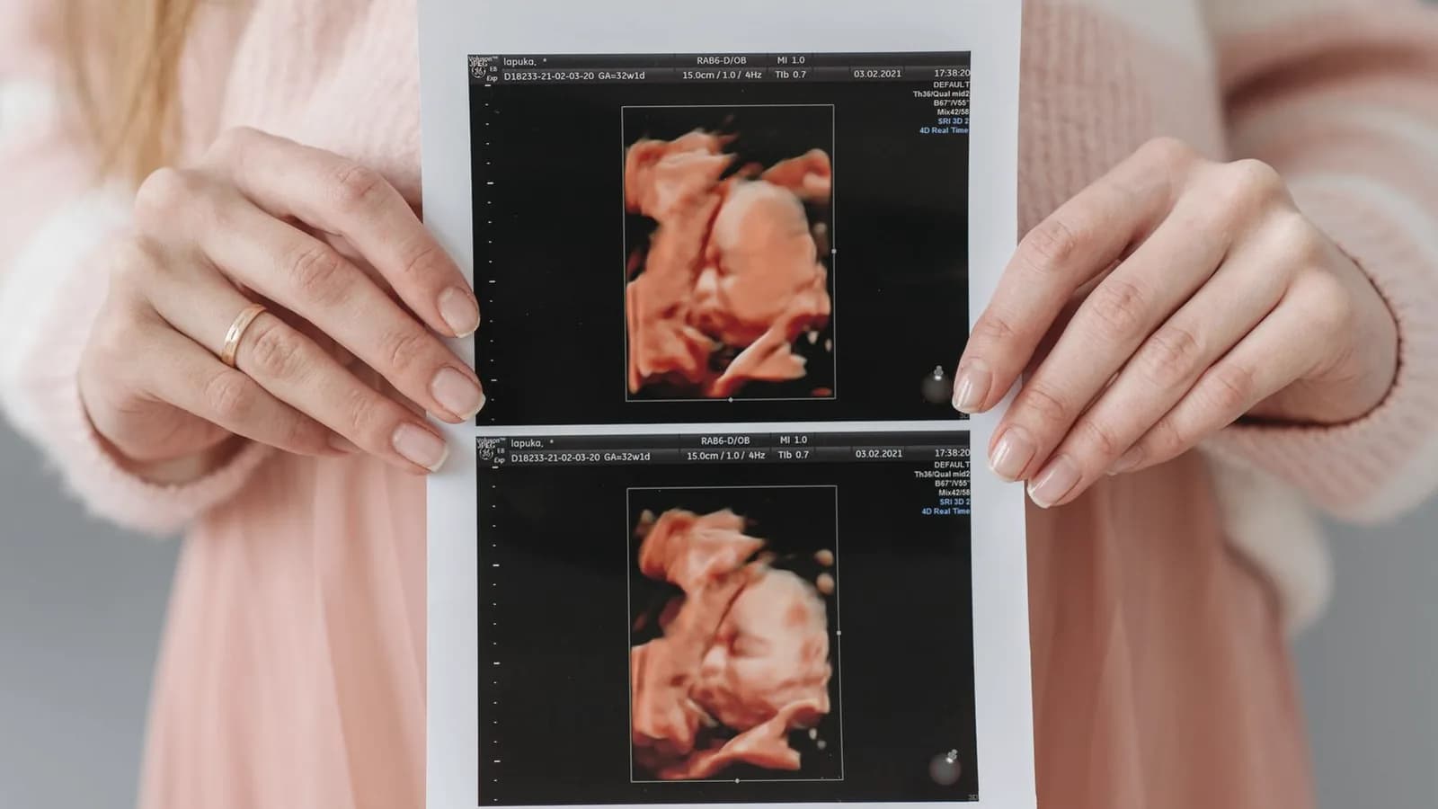 Expecting mother holding a printed 3D ultrasound picture of her baby against a soft pink dress