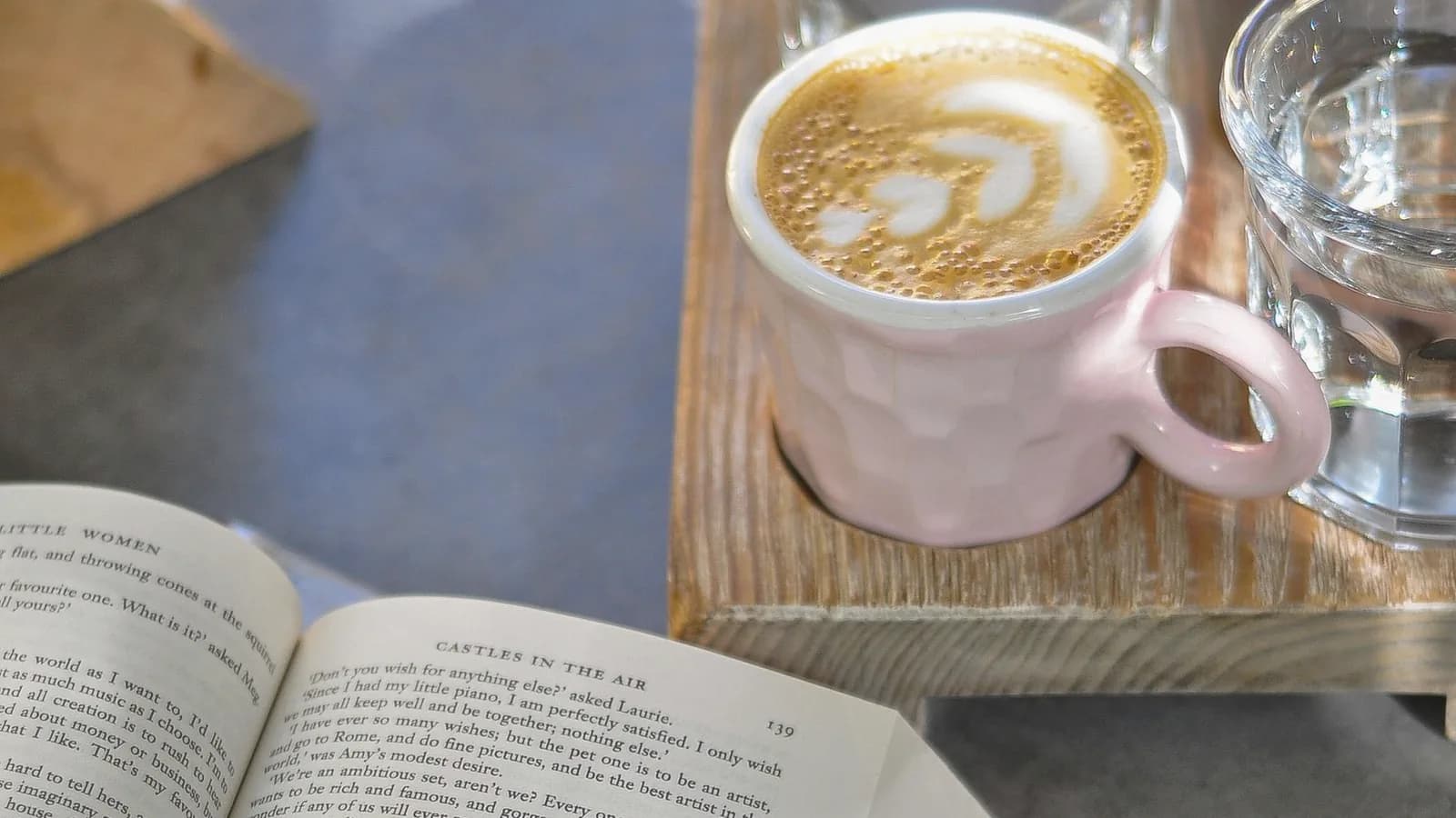 Caffeine and sugar during pregnancy: Latte with foam art beside an open book and a pink dessert plate