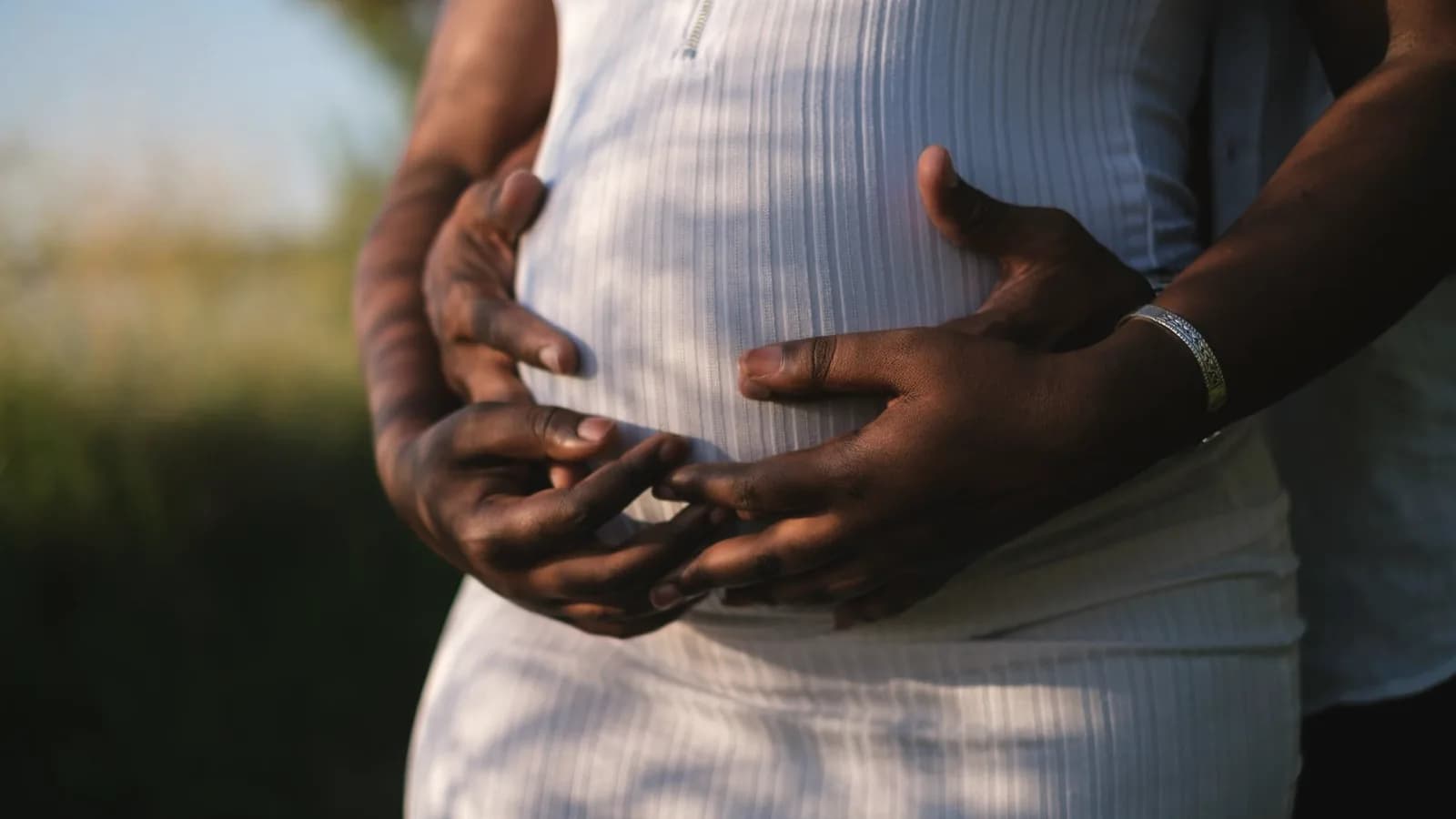 Can you see gender at 16 weeks: Couple's hands cradling a pregnant belly in a white dress outdoors