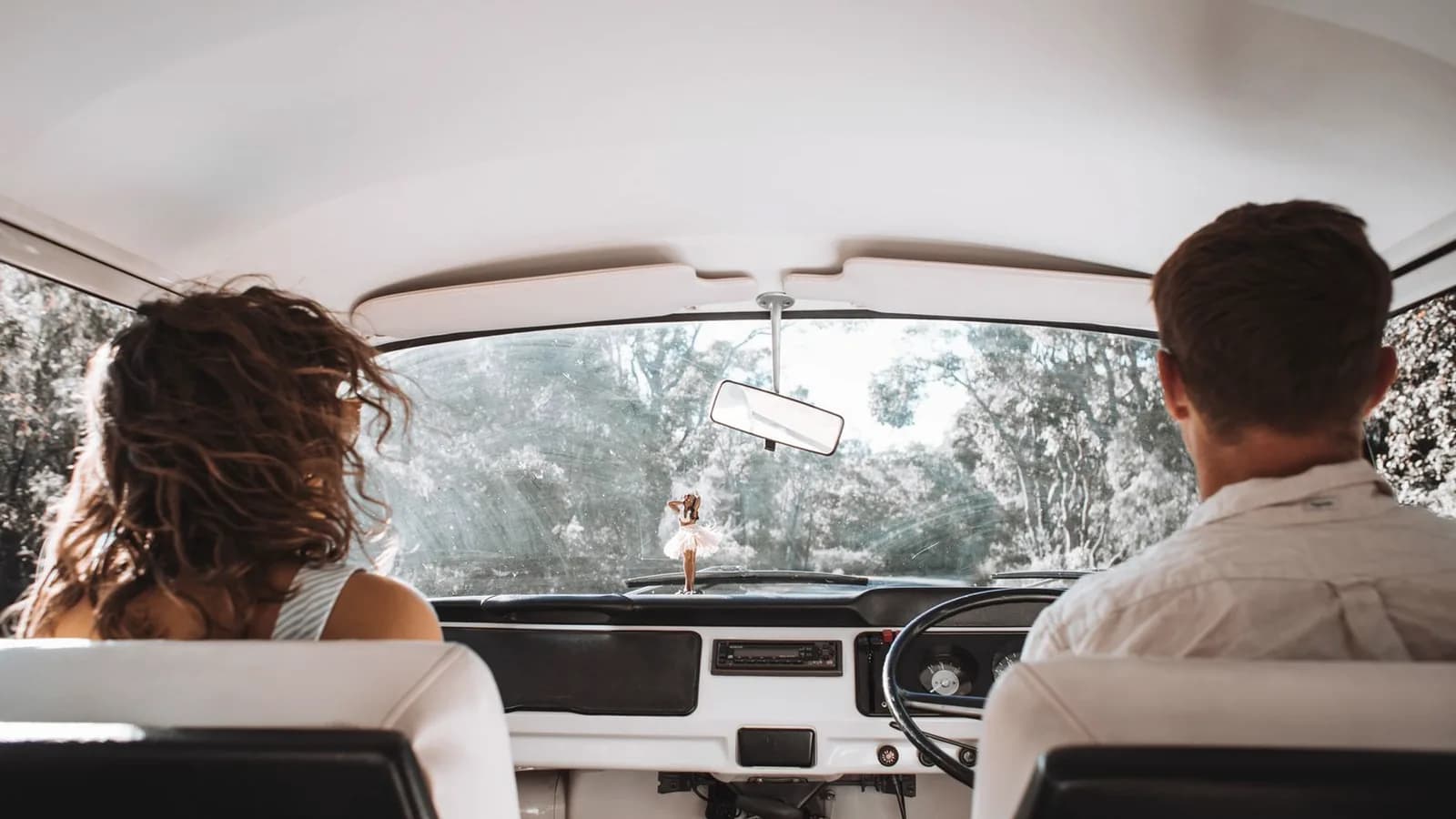 Couple seen from behind riding together in a vintage car on a sunny country drive