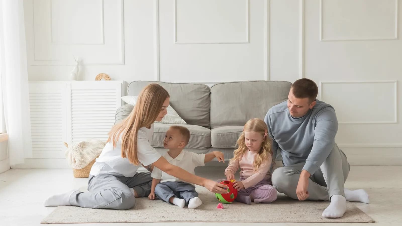Family ultrasound session with siblings: Family of four playing together on a rug in a bright cream living room