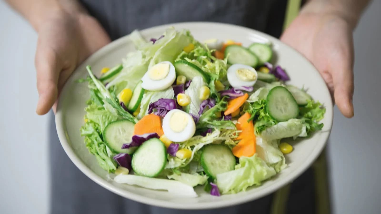 First trimester nutrition foods: Hands holding a plate of fresh salad with egg, cucumber, carrot and lettuce