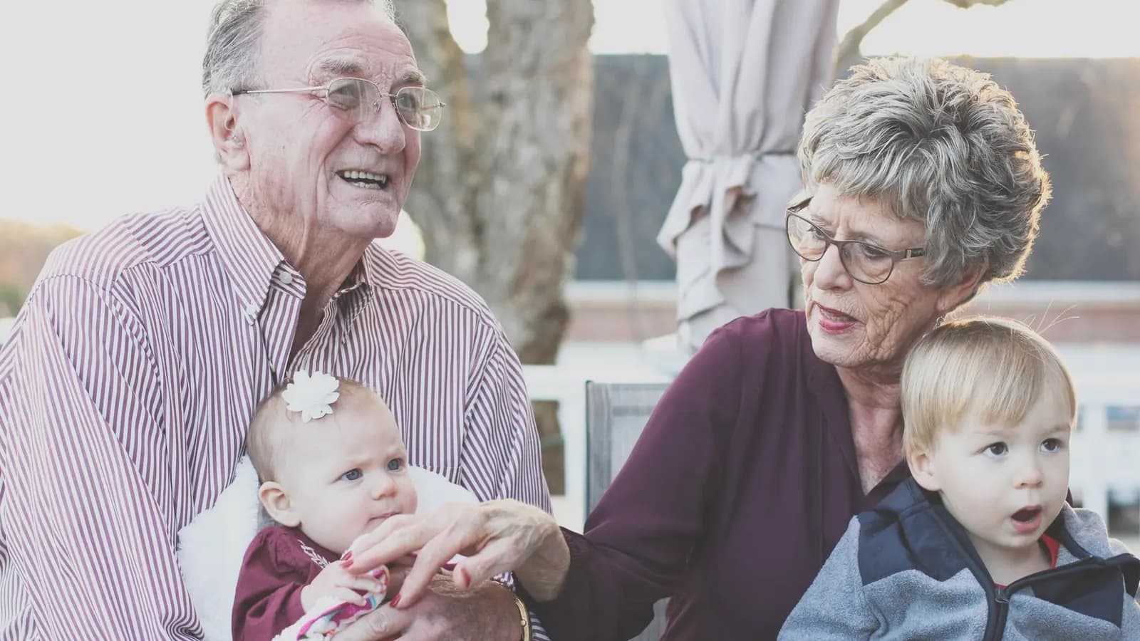 Grandparent ultrasound gift: Smiling grandparents holding two young grandchildren on their laps outdoors