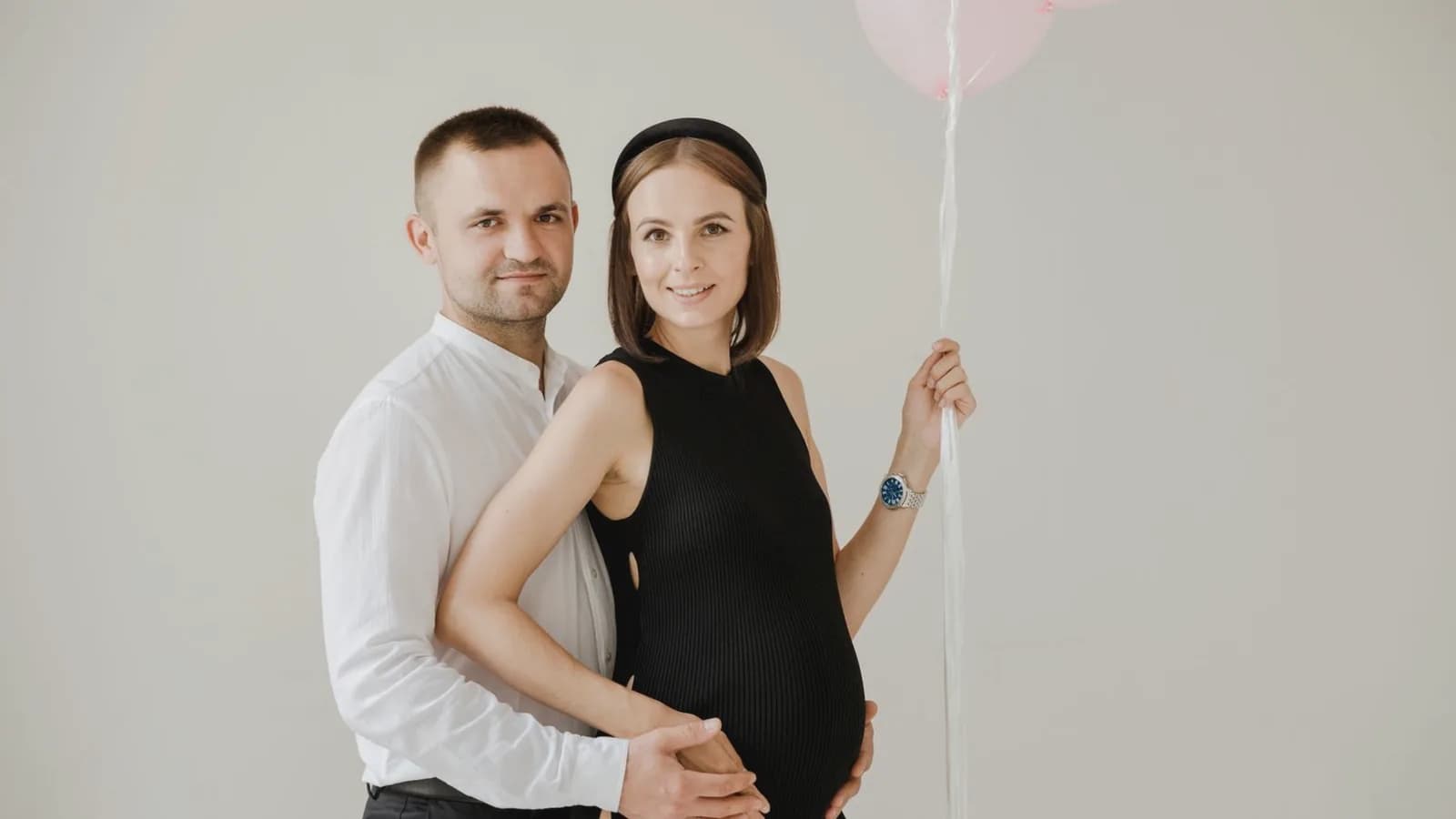 Intimacy during pregnancy: Expecting couple embracing tenderly with pale pink balloons in a soft light studio