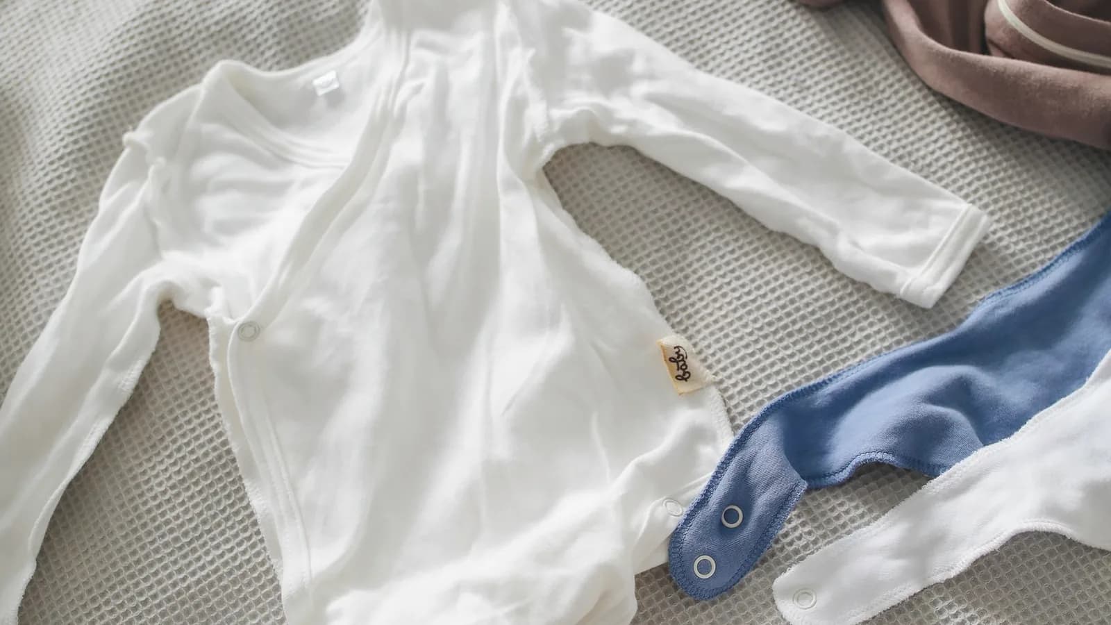 Old wives tales baby gender: Soft baby clothes and knitted hats arranged on a light bed