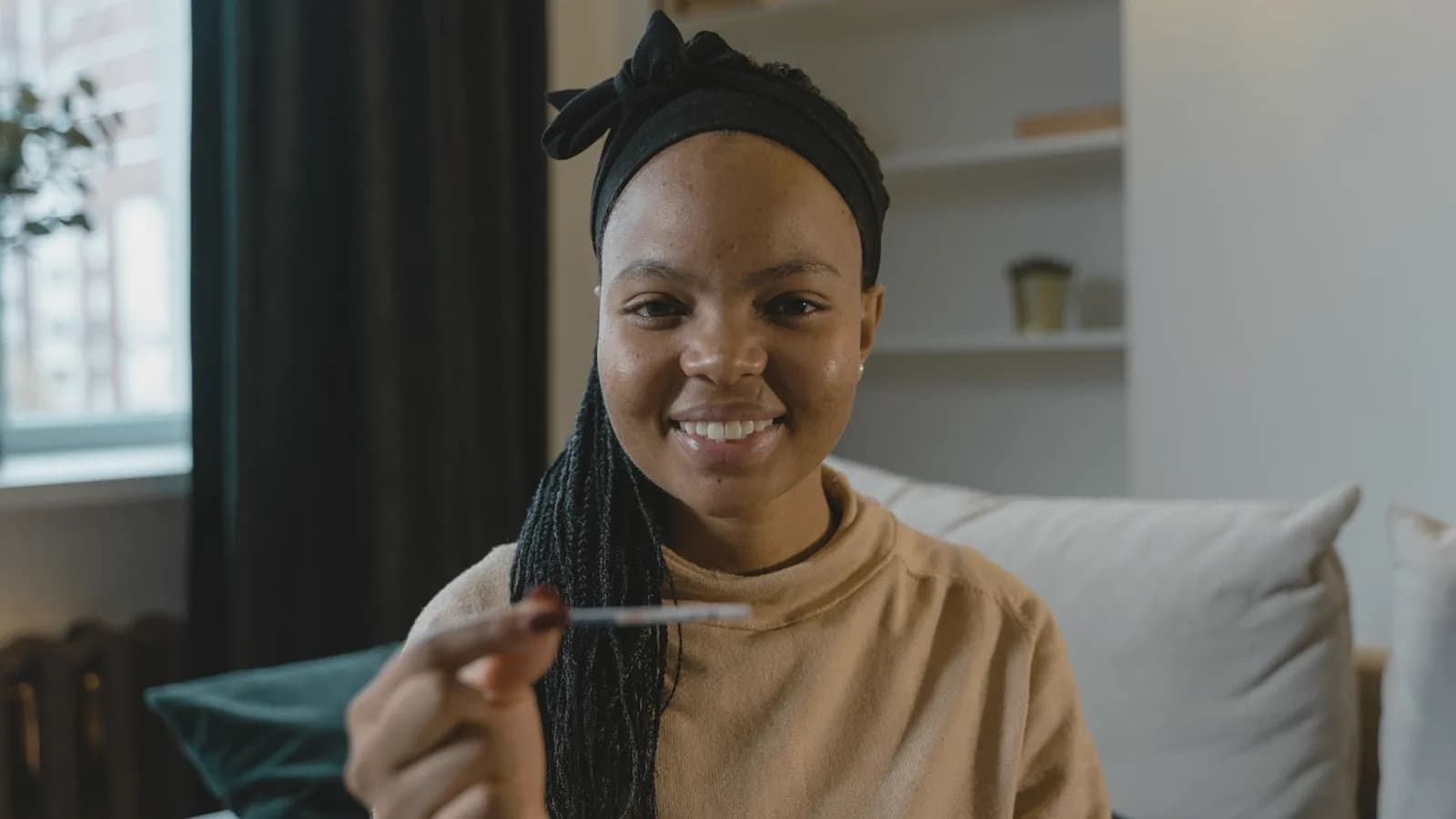 Pregnancy hormones and mood swings: Smiling woman on a sofa holding up a pregnancy test in a calm living room