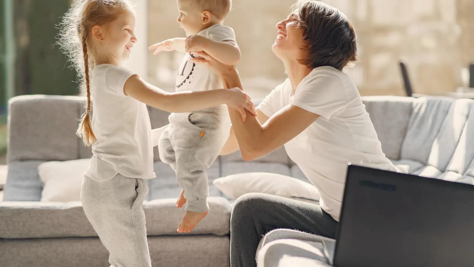Prenatal services in Durham: Smiling mother playing with two young children on a bright living room sofa