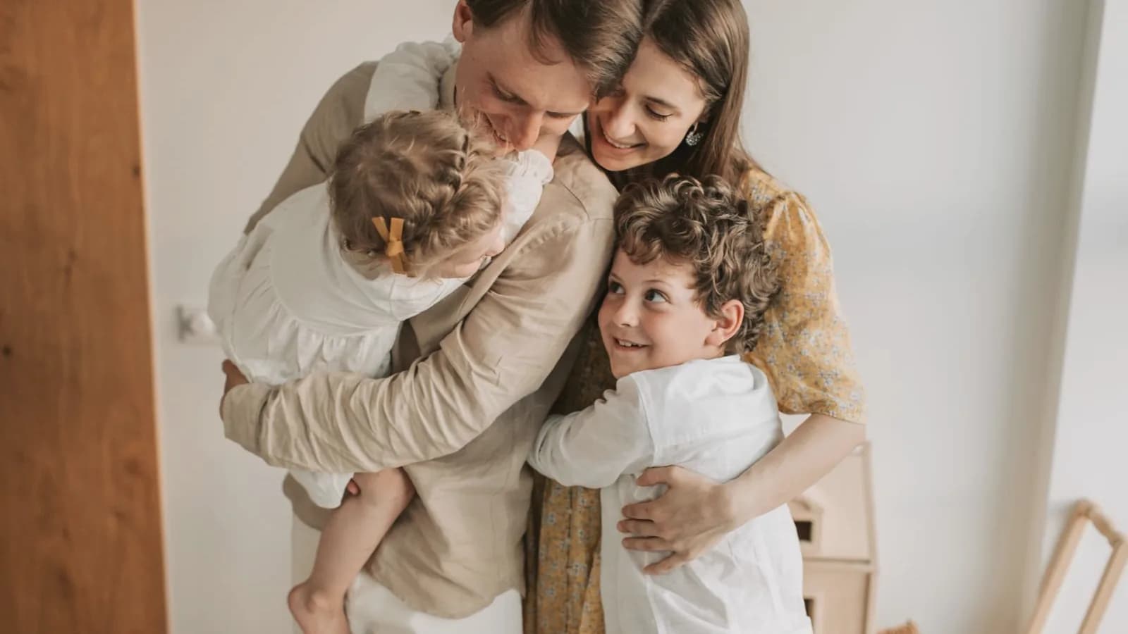 Prepare older sibling for new baby: Parents hugging their toddler daughter and older son in a warm bright room