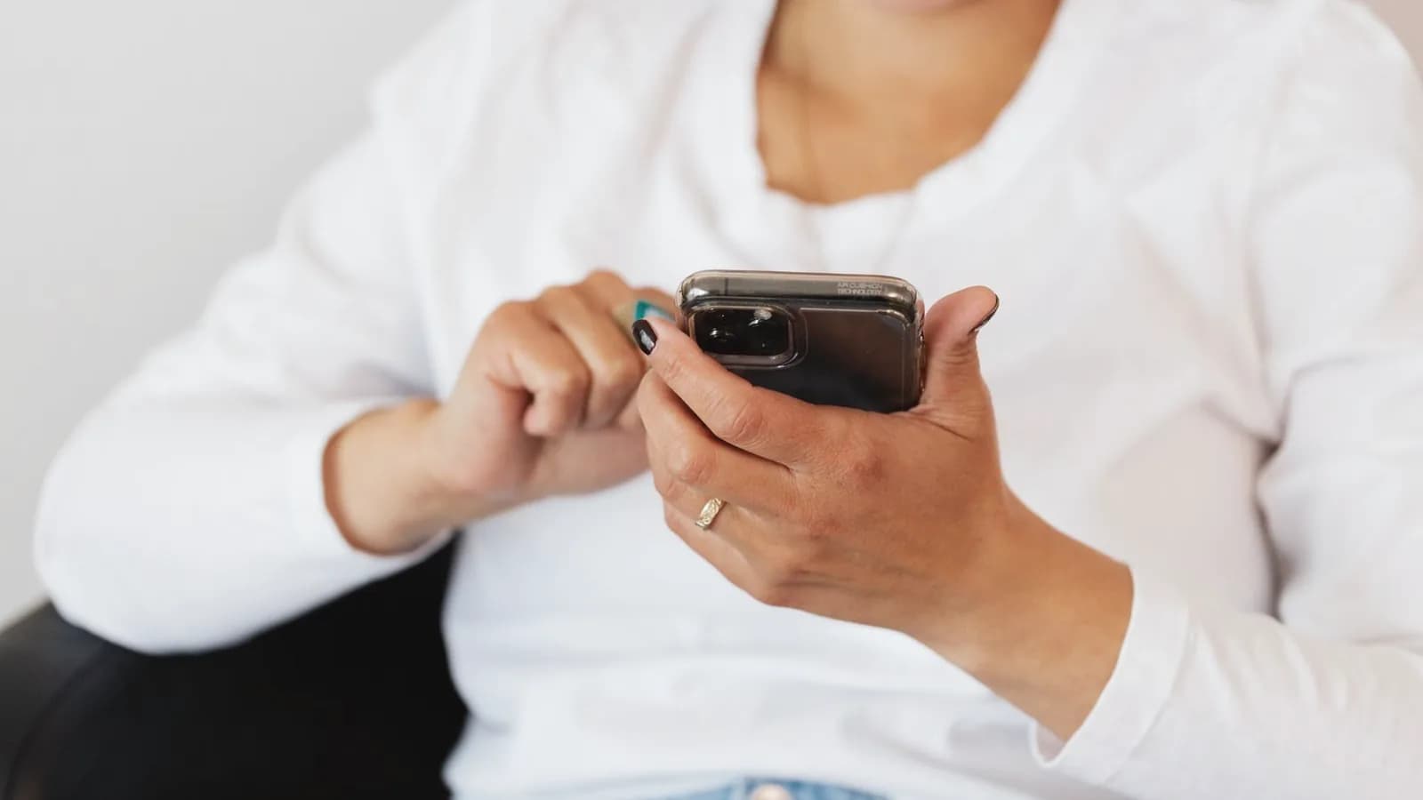 Share ultrasound photos on social media safely: Woman in a white top holding a smartphone while scrolling through photos