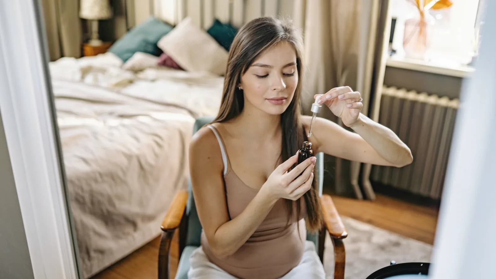 Skin changes during pregnancy: Pregnant woman applying a skincare serum with a dropper in a cozy bedroom