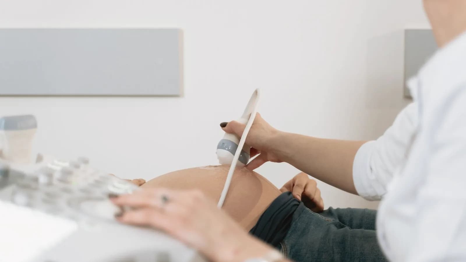 Ultrasound frequency and image quality: Sonographer gently moving an ultrasound probe over a pregnant belly in a bright room