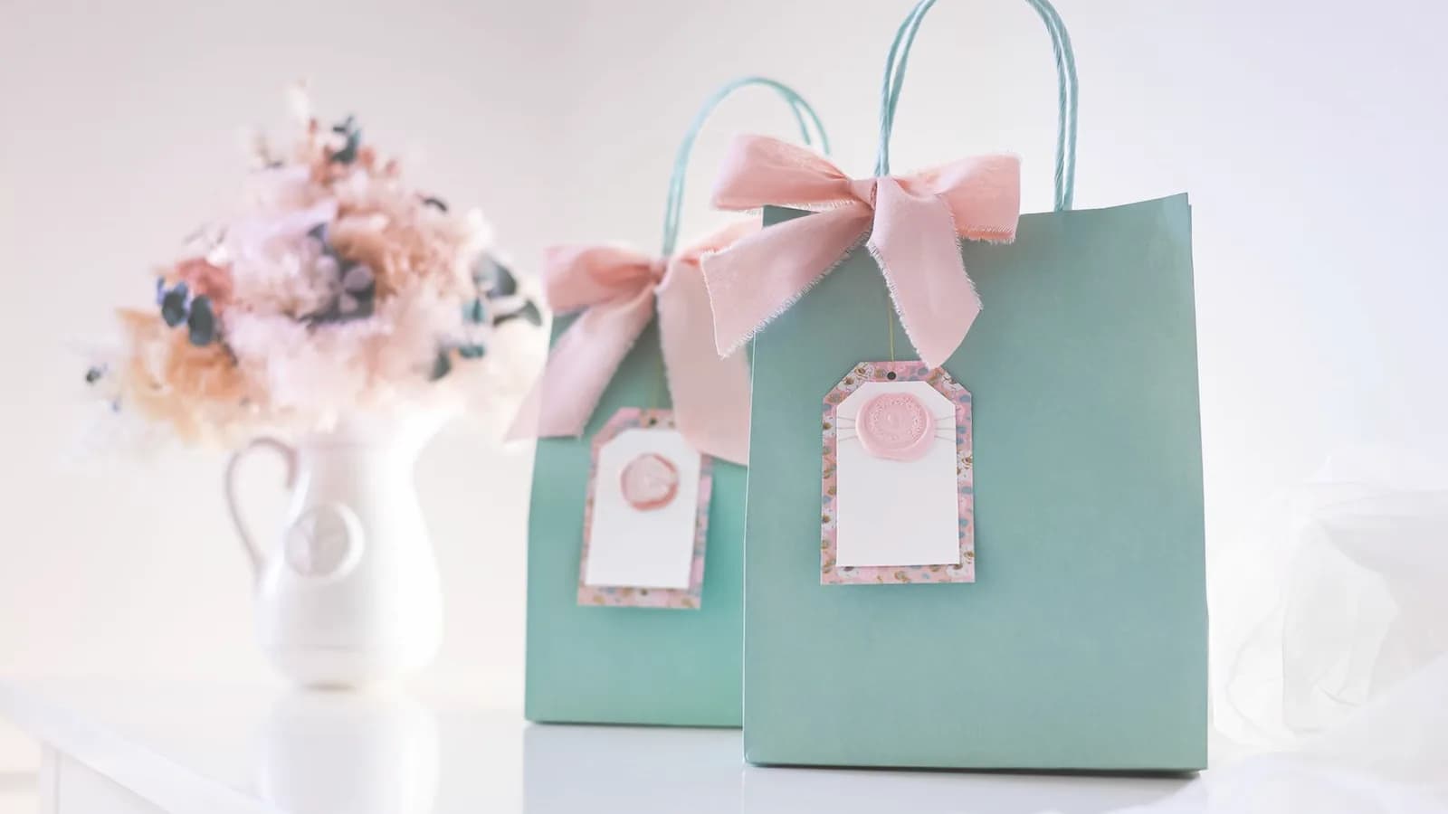 Ultrasound gift certificate for baby shower: Two sage green gift bags with pale pink bows beside a vase of soft flowers