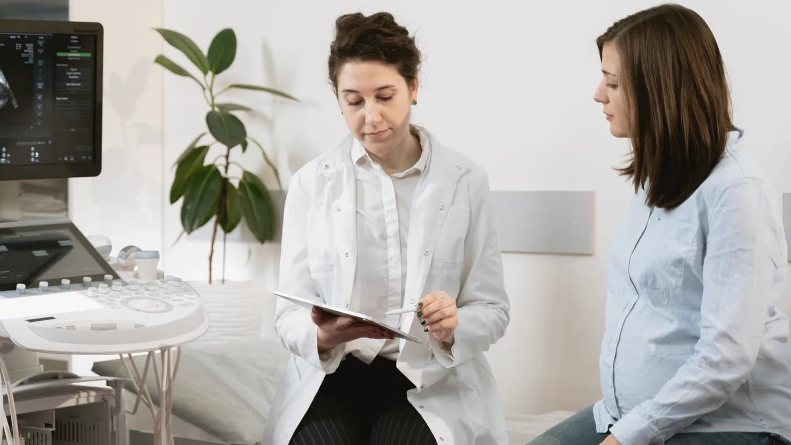 Ultrasounds by trimester: Doctor with tablet talking to a pregnant woman beside an ultrasound machine