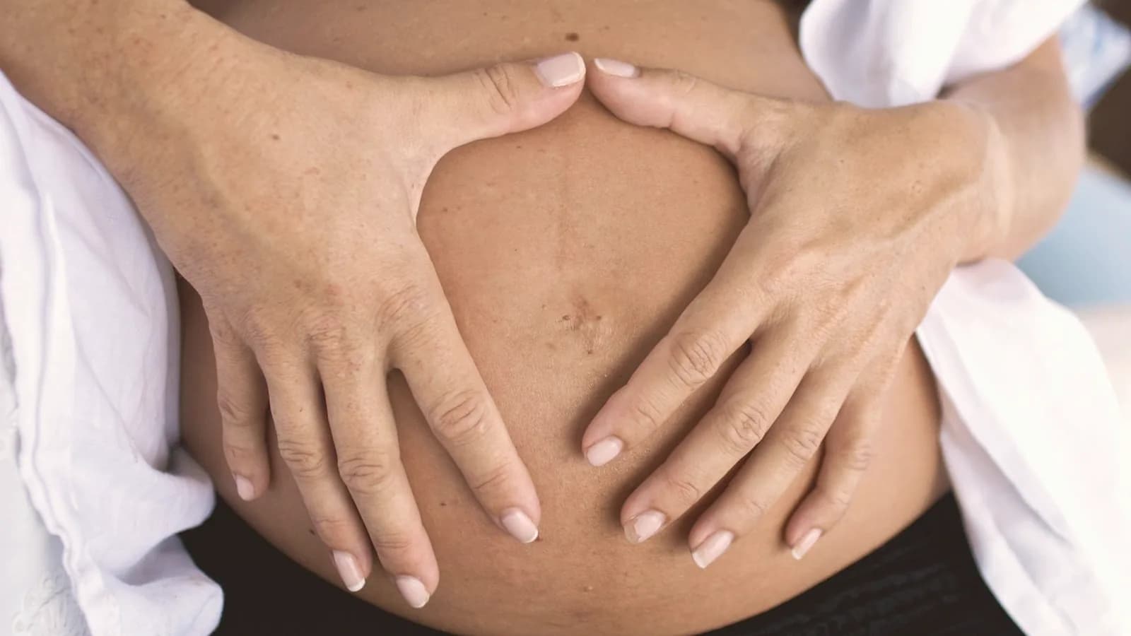 Week 8 ultrasound heartbeat: Close up of a warm pregnant belly with hands forming a heart shape