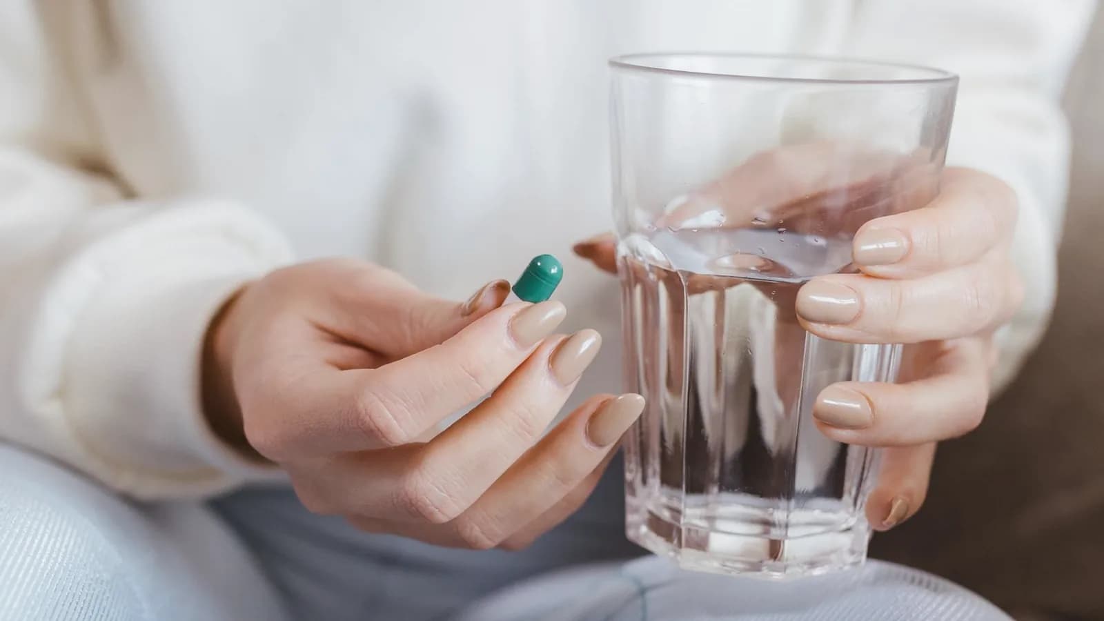 What prenatal vitamins do you really need: Woman in a cream sweater holding a green capsule and a glass of water