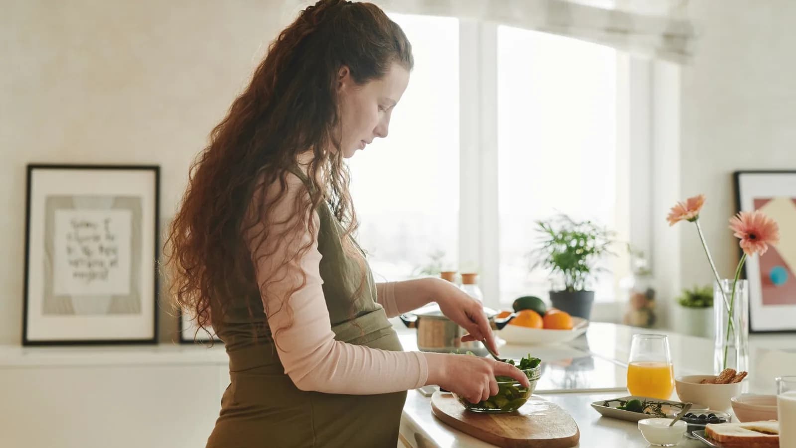 What to eat during pregnancy: Pregnant woman preparing fresh fruit and vegetables in a bright sunny kitchen