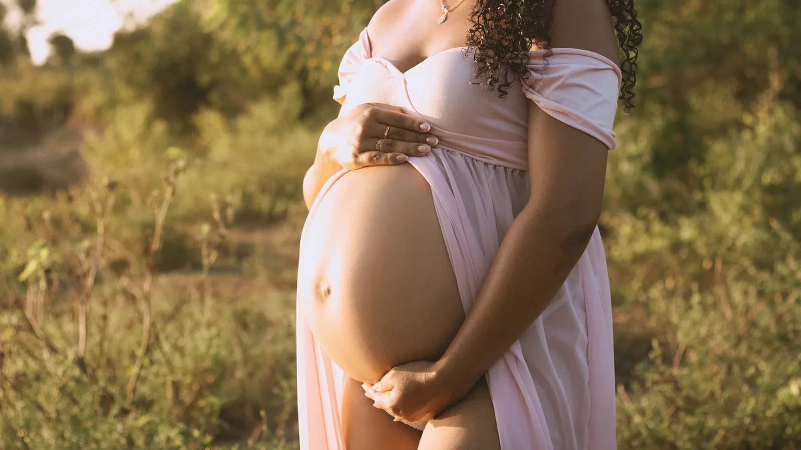 What to wear to a 3D ultrasound appointment: Pregnant woman in a soft pink off-shoulder dress cradling her belly in warm