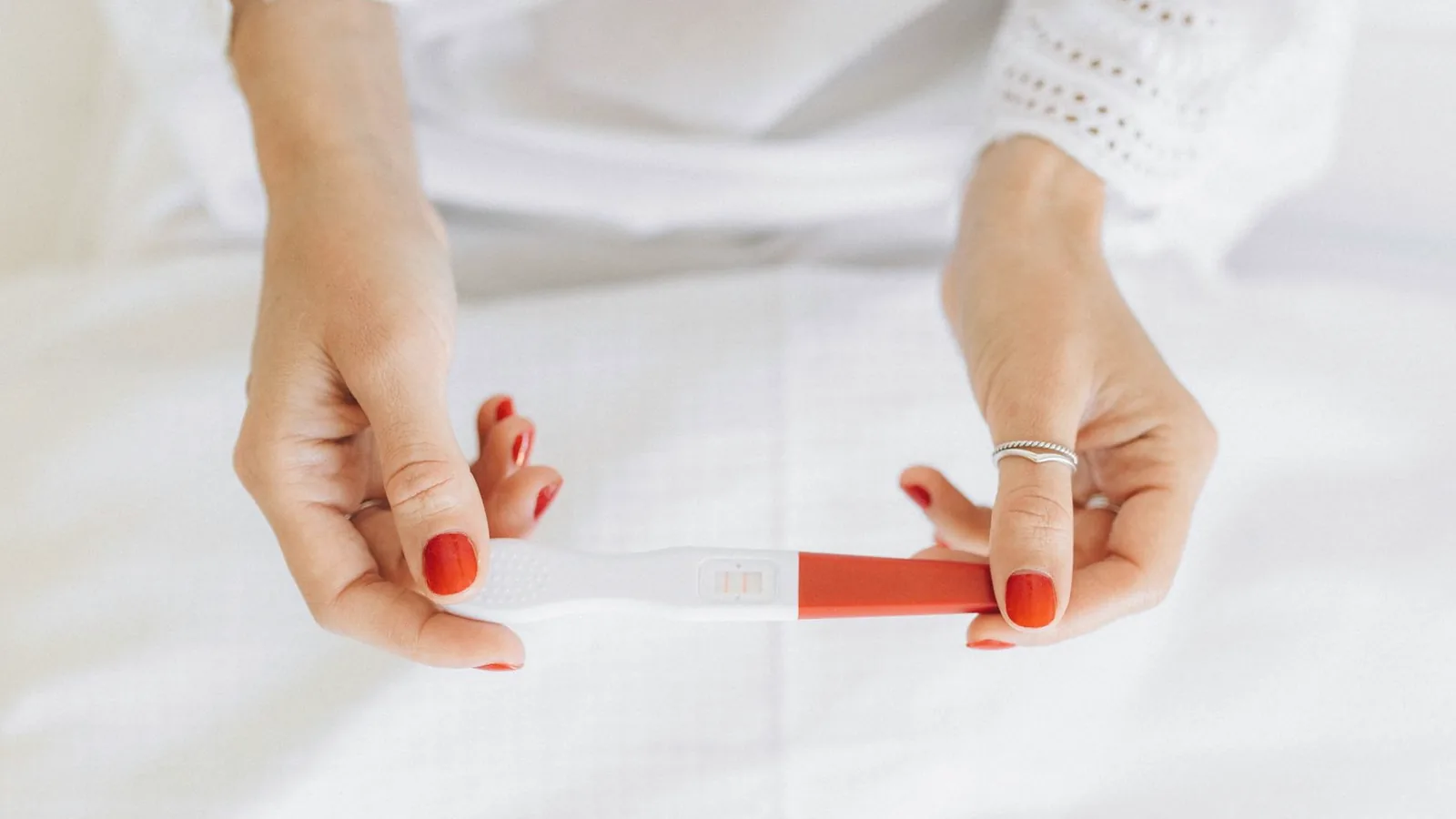 12 week ultrasound: Woman in white holding a positive pregnancy test in soft bright light
