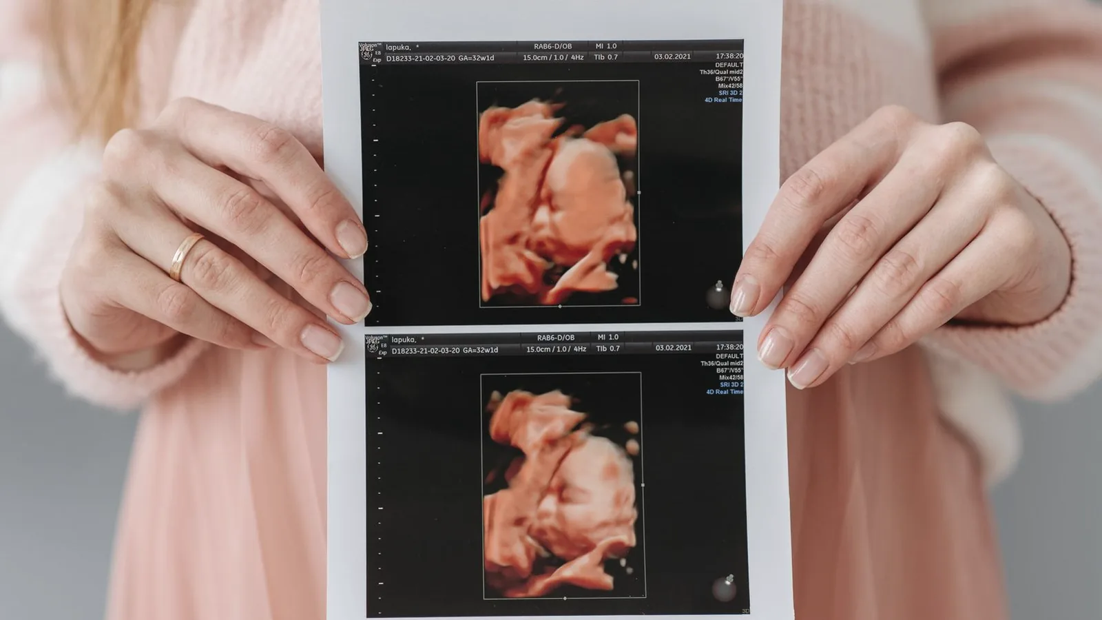 Expecting mother holding a printed 3D ultrasound picture of her baby against a soft pink dress