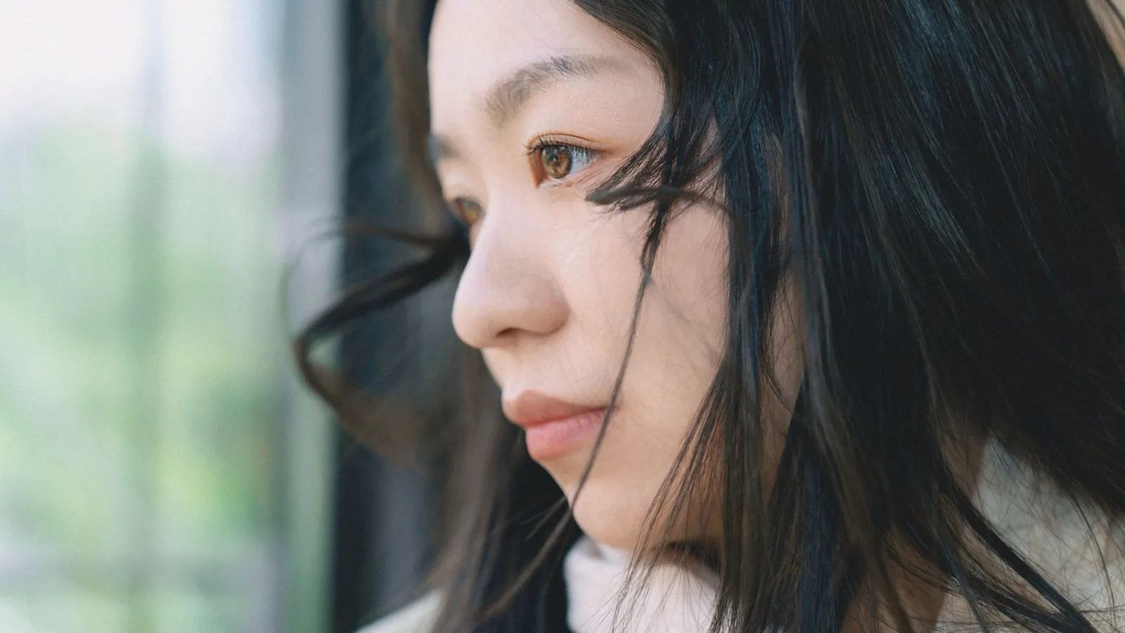 Anxiety during pregnancy: Thoughtful young woman gazing out a window in soft natural light