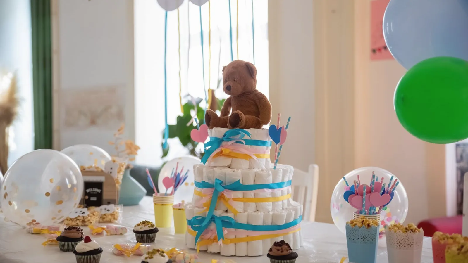 Baby shower table with diaper cake, cupcakes, balloons and pastel decorations in a bright room