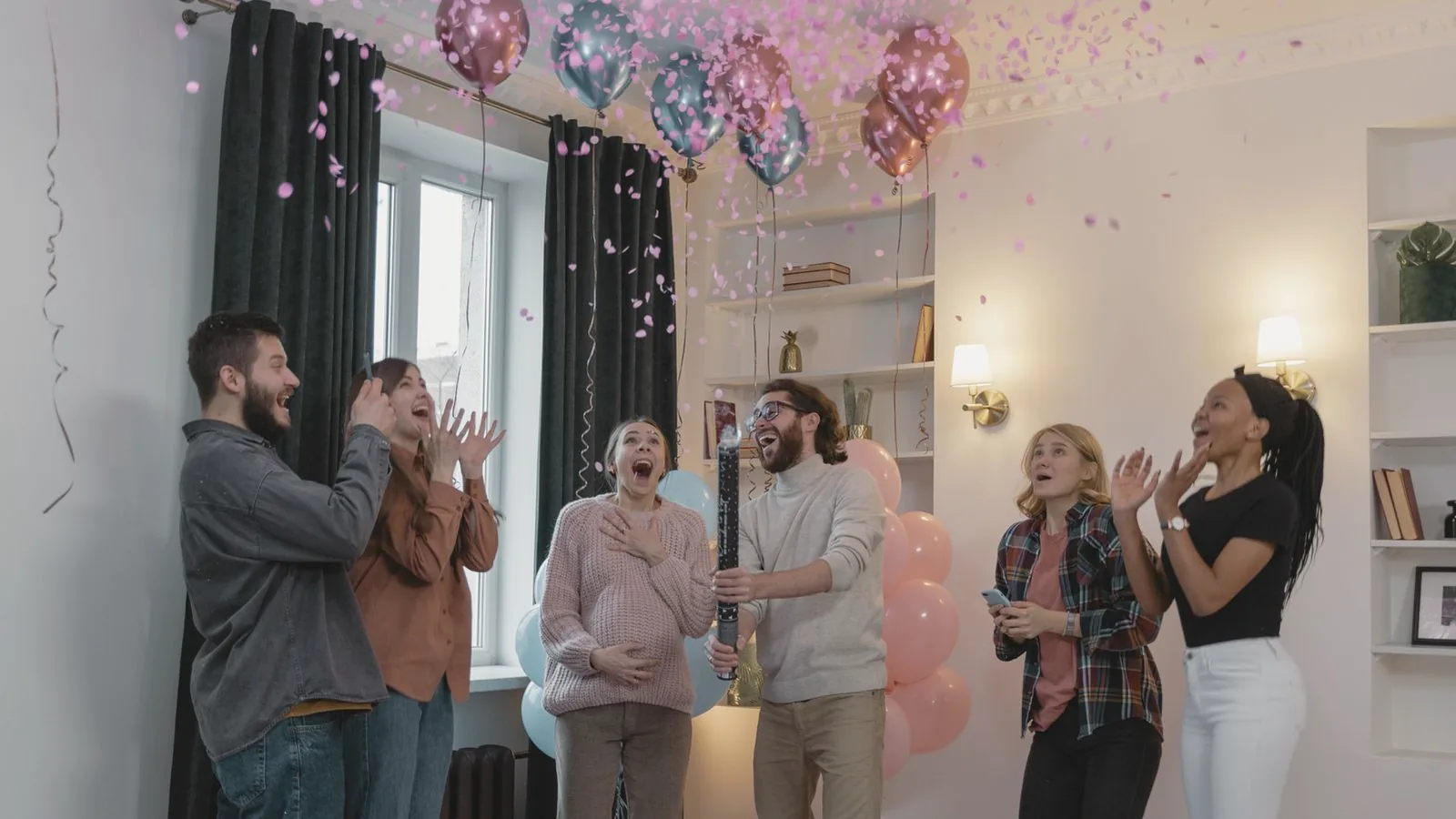 Creative gender reveal ideas: Excited friends and an expecting mother cheer as pink confetti bursts over balloons at a