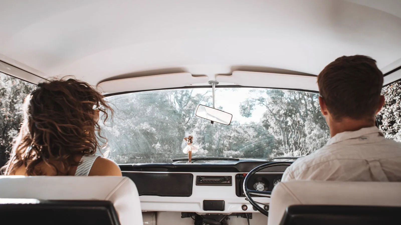 Couple seen from behind riding together in a vintage car on a sunny country drive