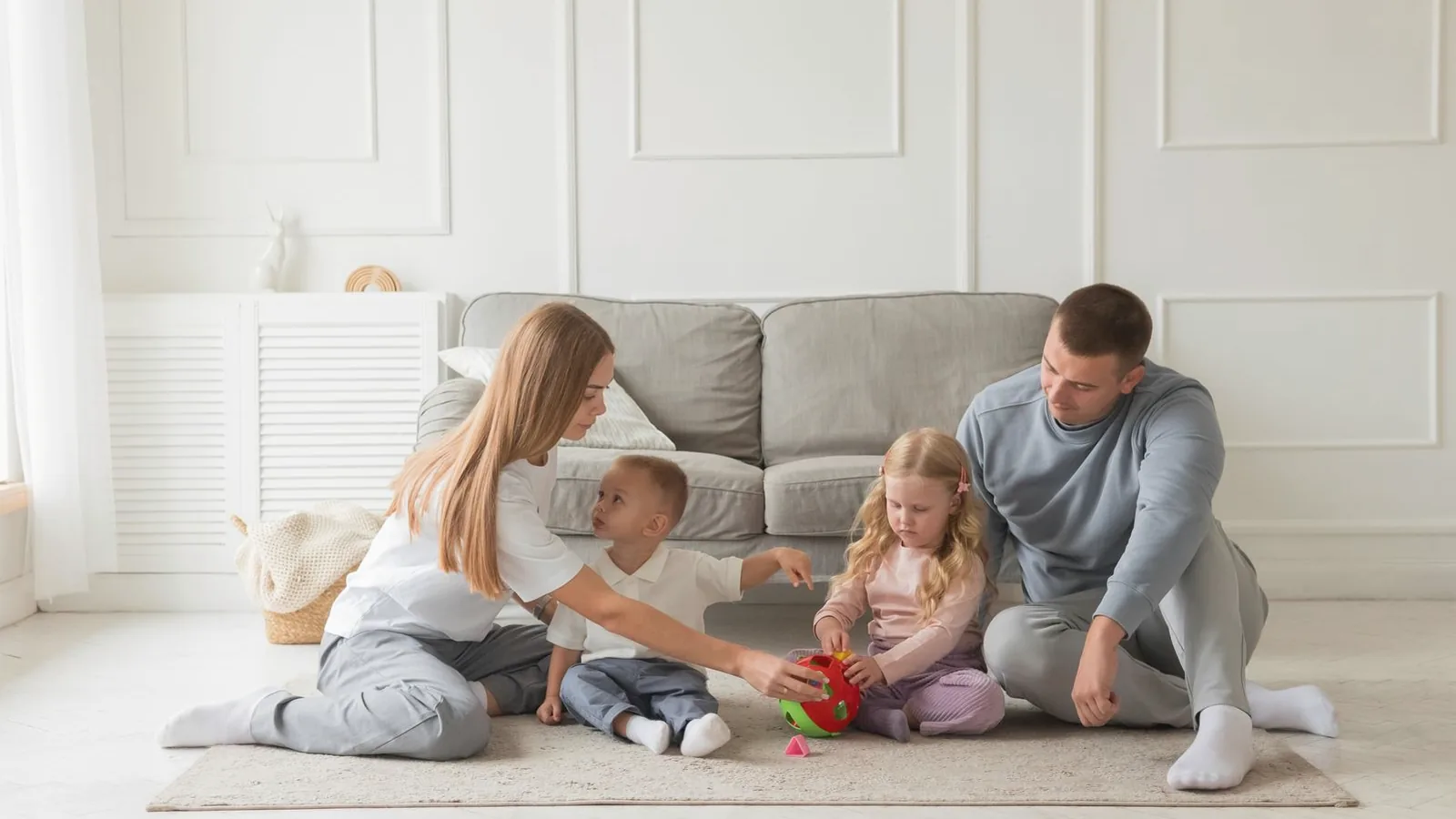 Family ultrasound session with siblings: Family of four playing together on a rug in a bright cream living room