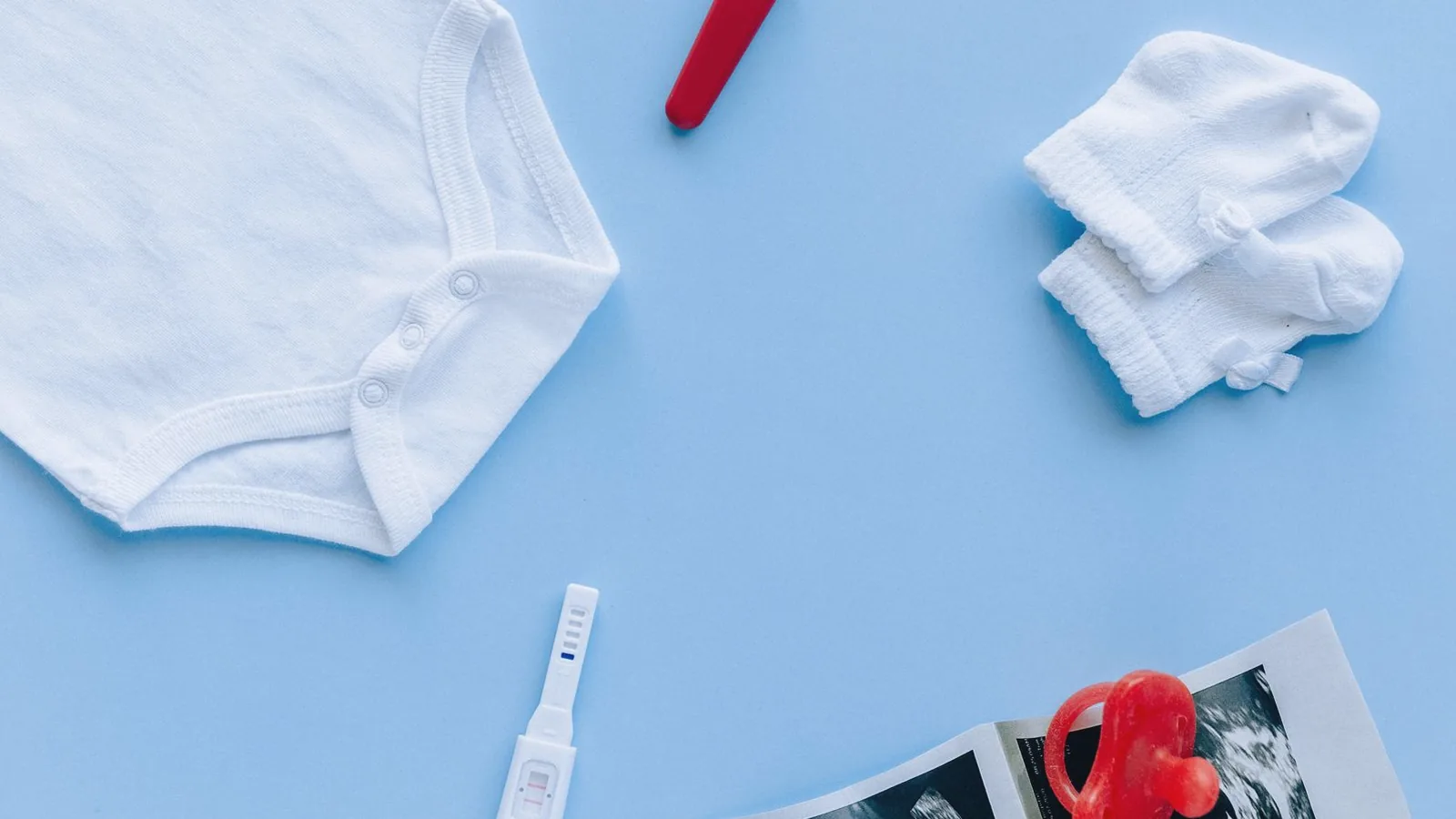 Find out baby gender: Flat lay of baby bodysuit, socks, pregnancy test and ultrasound prints on blue