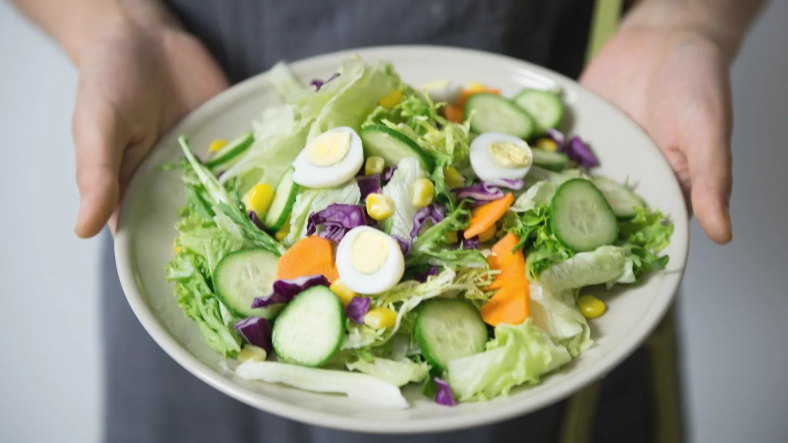 First trimester nutrition foods: Hands holding a plate of fresh salad with egg, cucumber, carrot and lettuce