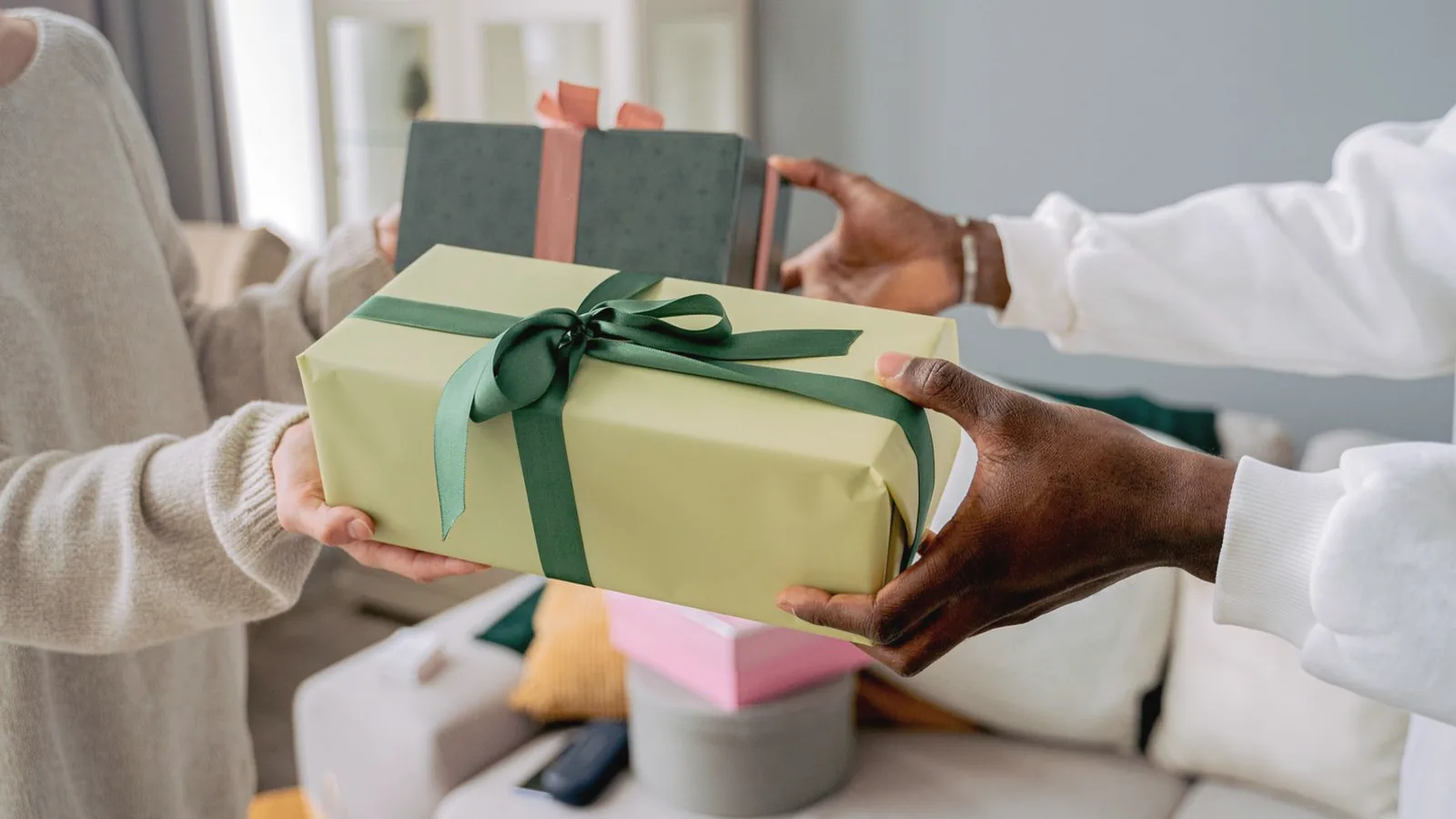 Gifts for expecting dads: Hands exchanging a sage green wrapped gift with a dark green ribbon