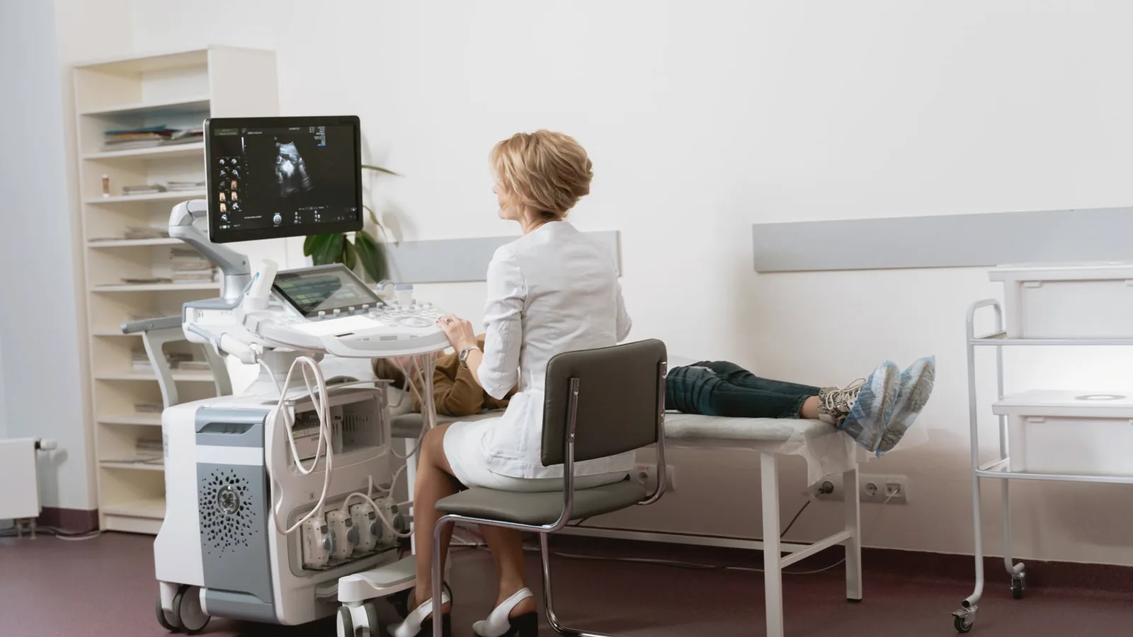 How ultrasound technology works: Sonographer at a modern ultrasound machine with patient resting in a bright clinic room