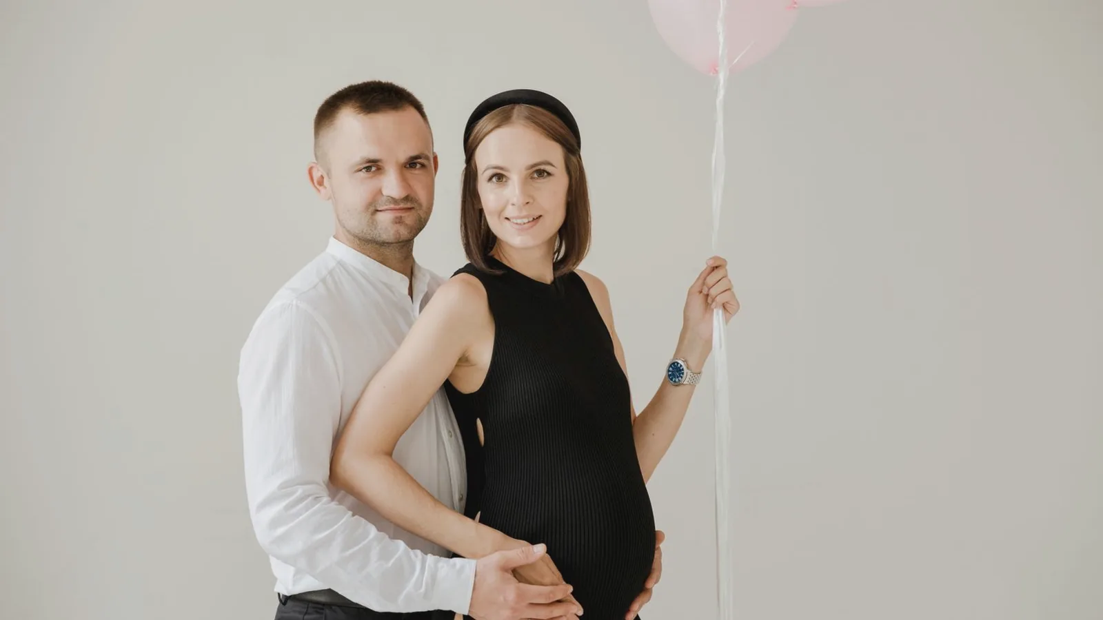 Intimacy during pregnancy: Expecting couple embracing tenderly with pale pink balloons in a soft light studio