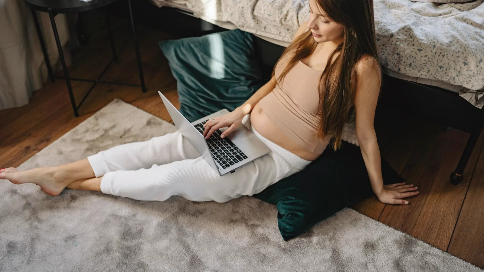 Maternity resources in Raleigh: Pregnant woman sitting on a rug in her bedroom looking up resources on a laptop
