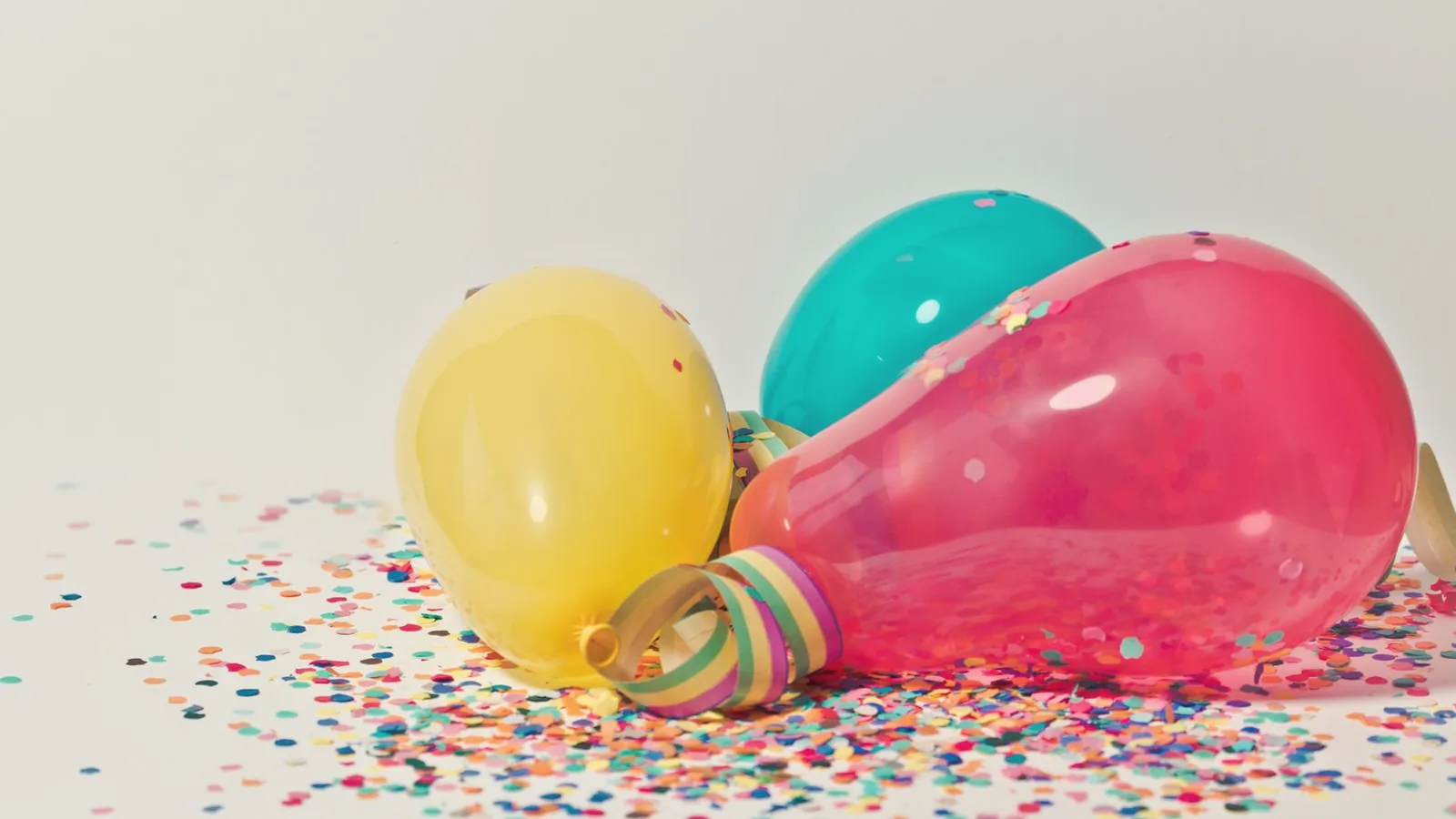 Plan a gender reveal party: Yellow, pink and teal party balloons among colorful confetti on a white surface
