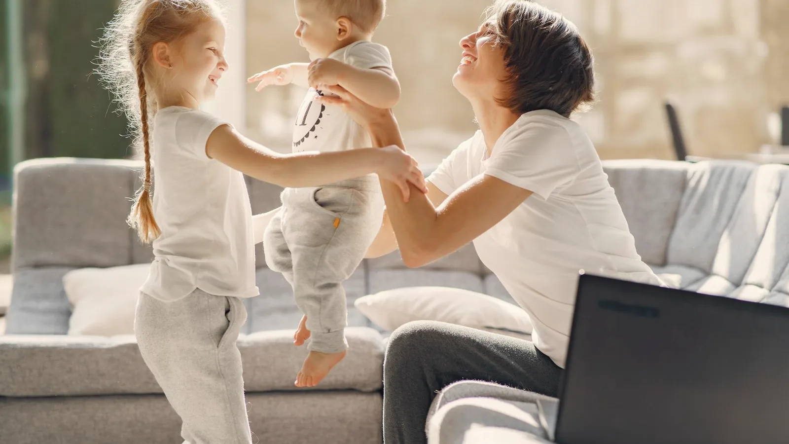 Prenatal services in Durham: Smiling mother playing with two young children on a bright living room sofa