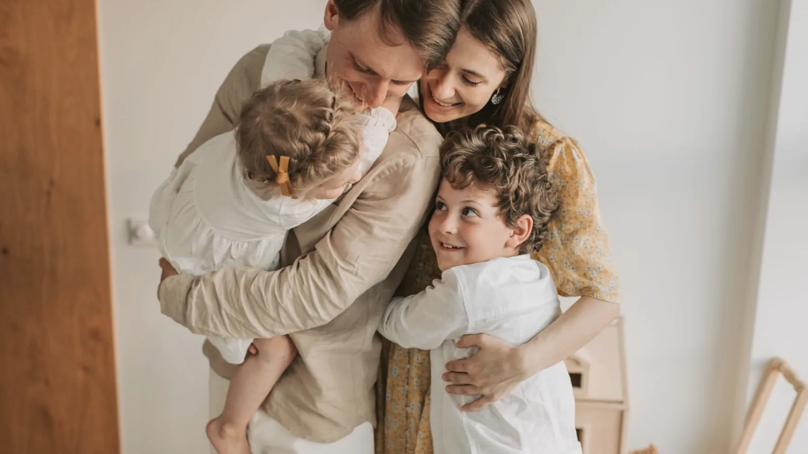 Prepare older sibling for new baby: Parents hugging their toddler daughter and older son in a warm bright room