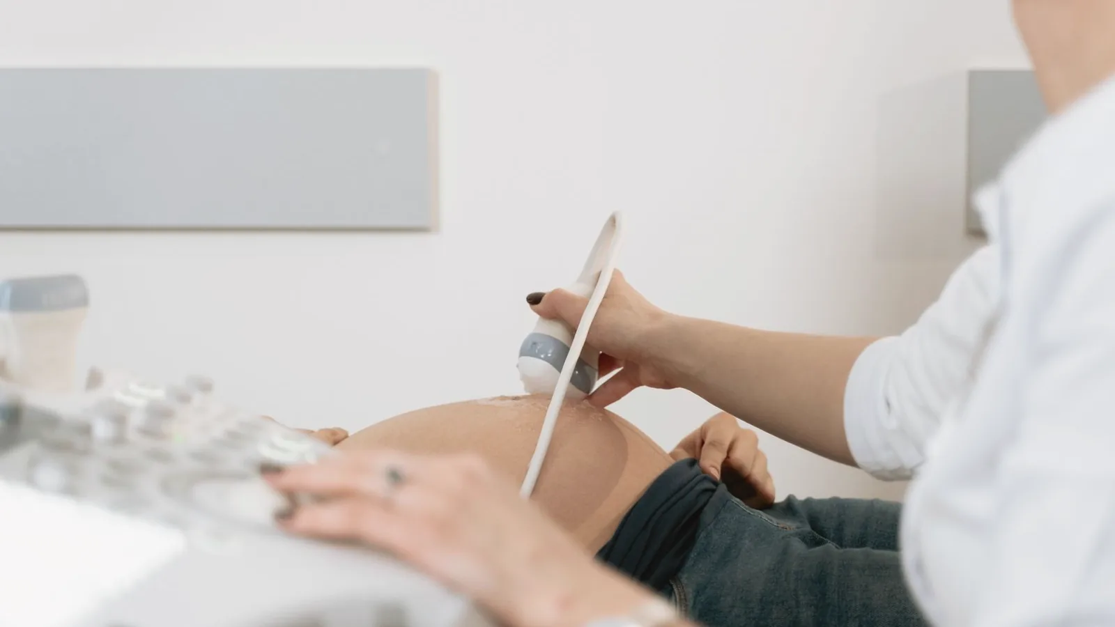 Ultrasound frequency and image quality: Sonographer gently moving an ultrasound probe over a pregnant belly in a bright room