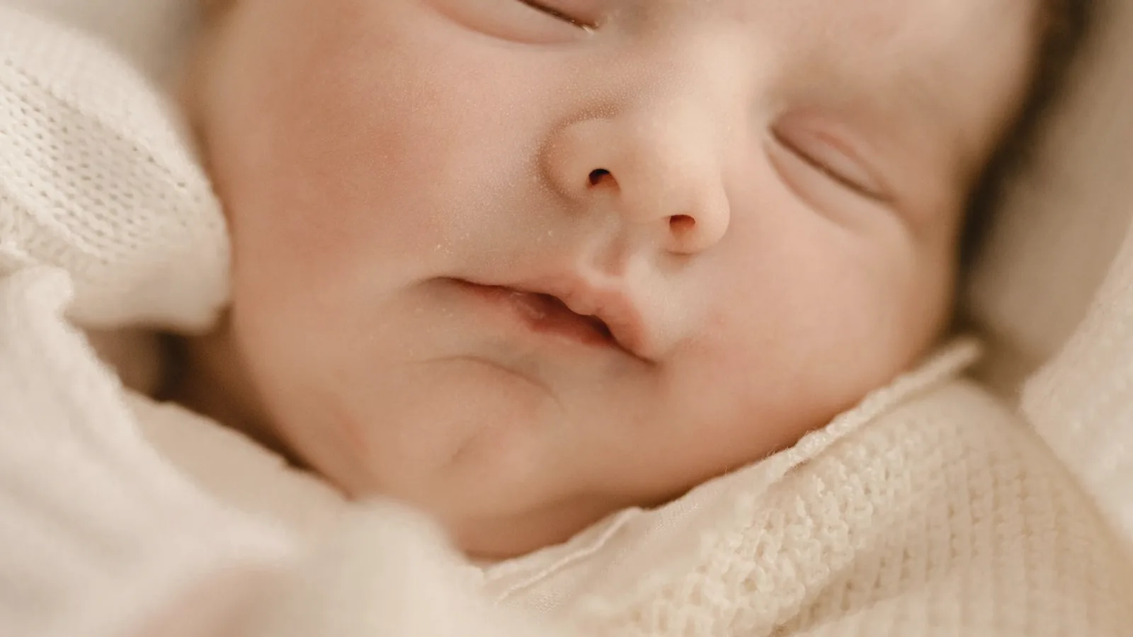 Why baby looks different on 3D ultrasound: Close up of a sleeping newborn face wrapped in a soft cream blanket